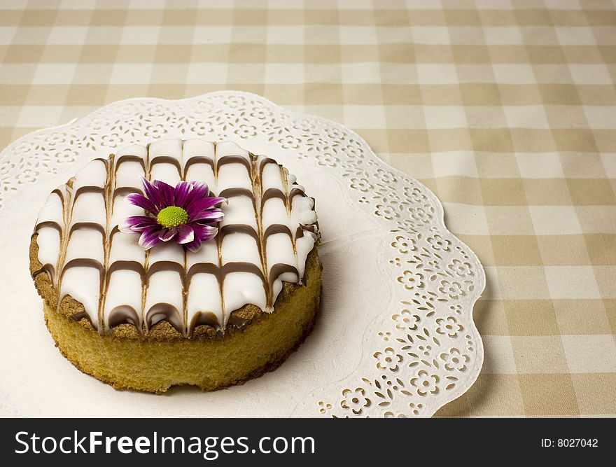 Baked fancy cake with a purple flower on a table with soft beige square cloth.