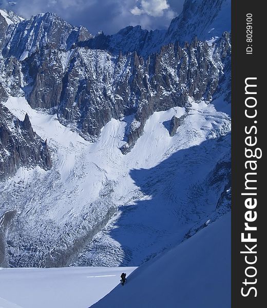 An man mounting a snowy slope of a tall mountain ridge. An man mounting a snowy slope of a tall mountain ridge