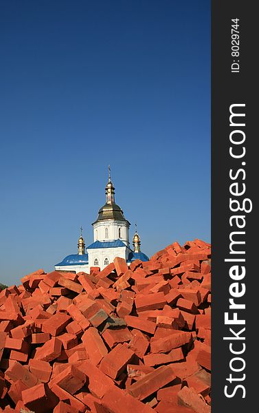 Renewed orthodox church over red bricks pile against deep blue sky. Renewed orthodox church over red bricks pile against deep blue sky