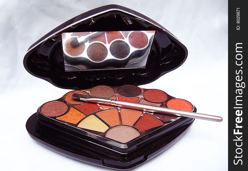 A makeup kit exposing various colored  eyeshadow, with a eyeshadow brush on the top. A makeup kit exposing various colored  eyeshadow, with a eyeshadow brush on the top