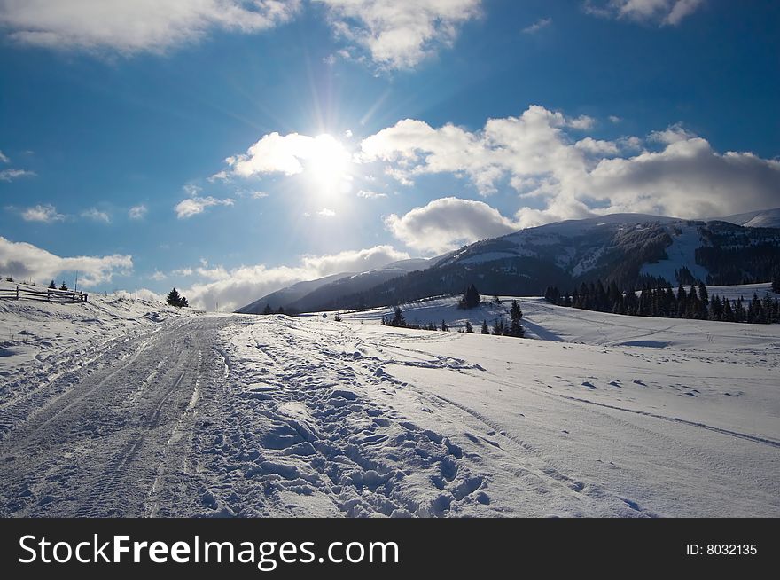 Winter mountains with bright sun on cloudy sky