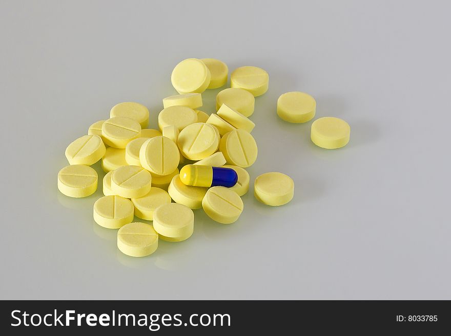 Pile of yellow pills and one blue and yellow capsule. Pile of yellow pills and one blue and yellow capsule