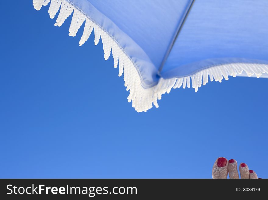 Red pedicure against clear blue sky and beach umbrella