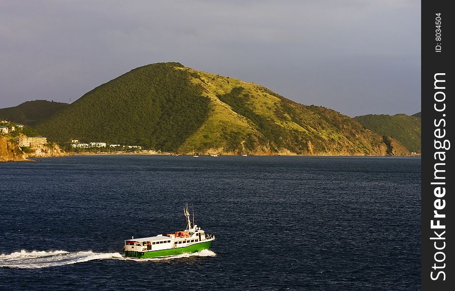 A green and white ferry boat sailing across the bay at a green island. A green and white ferry boat sailing across the bay at a green island