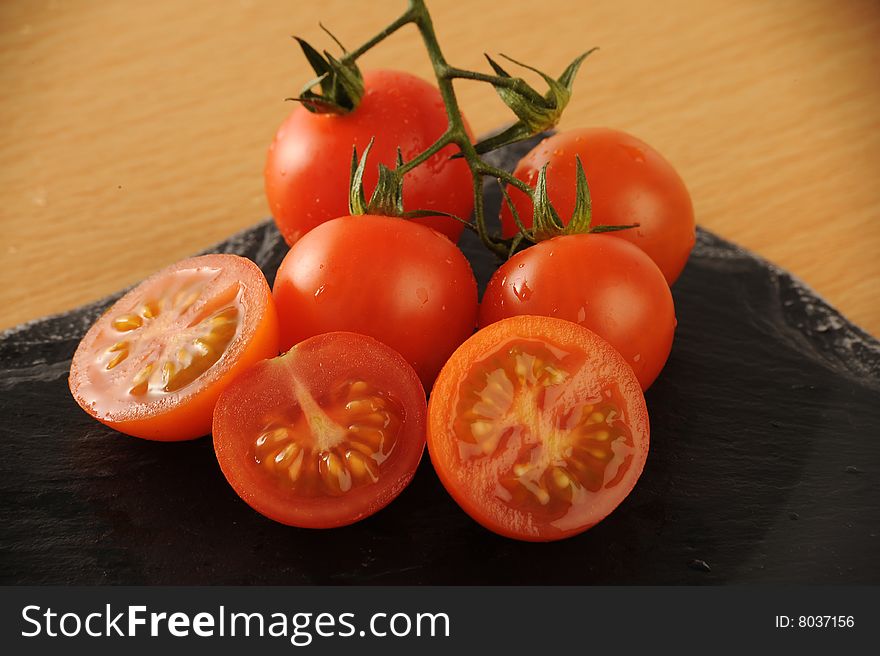 Group of fresh Cherry Tomatoes, some sliced, some whole on a black surface