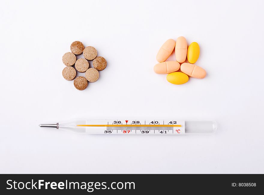 Pills piles with a thermometer on white background