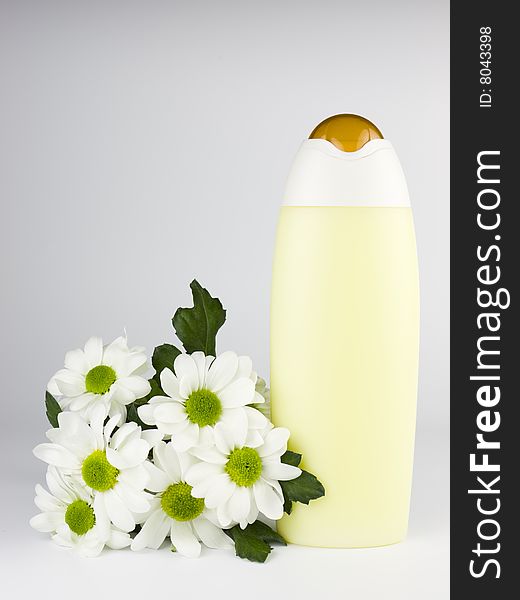 Bath cosmetics - a detail of a yellow shampoo or body lotion bottle with white flowers and copy space.