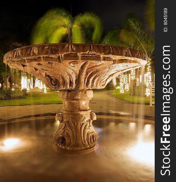 Water flowing from illuminated fountain at night in luxury resort, illuminated palm trees in background. Water flowing from illuminated fountain at night in luxury resort, illuminated palm trees in background