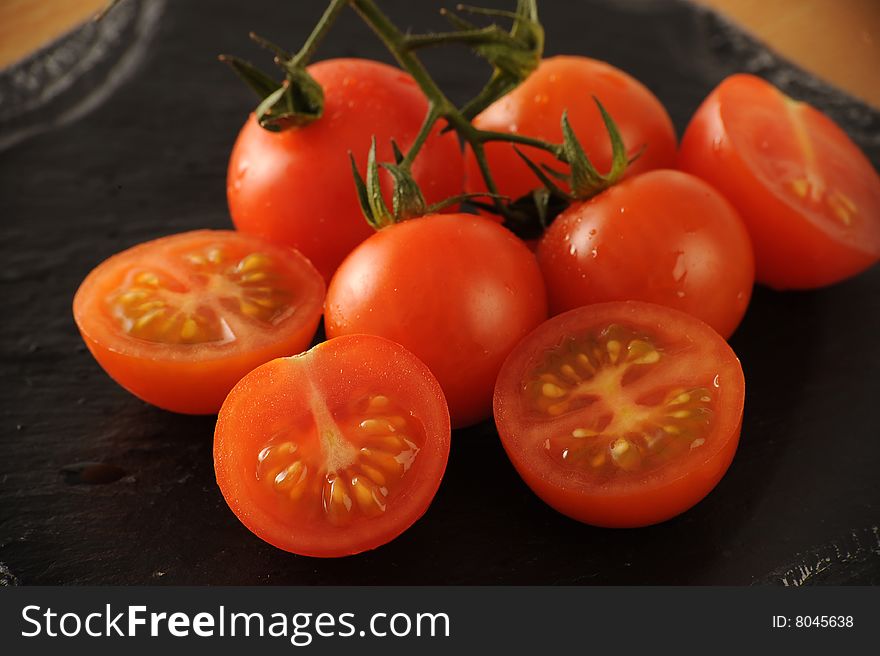 Group of fresh Cherry Tomatoes, some sliced, some whole on a black surface