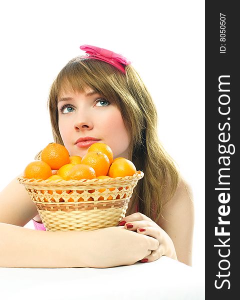 Beautiful dreamy young woman sitting by the table with a basket full of tangerines standing on it. Beautiful dreamy young woman sitting by the table with a basket full of tangerines standing on it