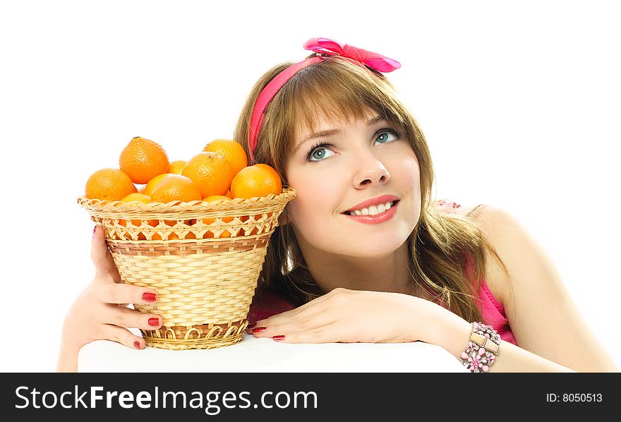 Beautiful young dreamy woman sitting by the table with a basket full of tangerines standing on it. Beautiful young dreamy woman sitting by the table with a basket full of tangerines standing on it