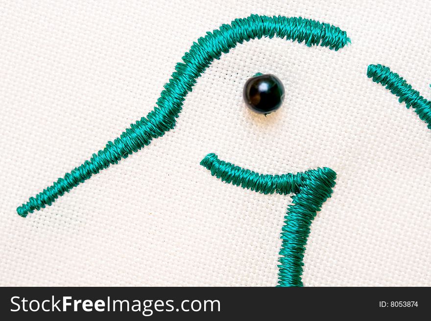 Closeup of embroidered bird head  green yarn  black button eye on white fabric