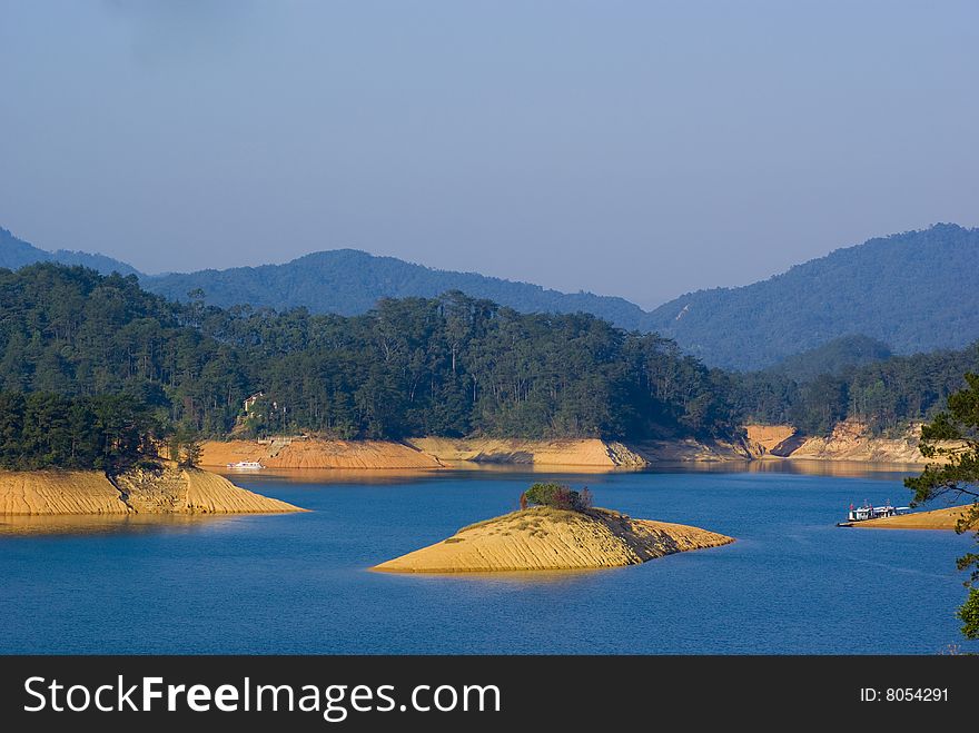 The landscape of reservoir with green mountain and exposed banks.