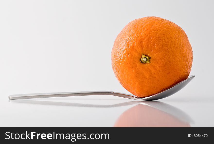 Metal tea-spoon with tangerine in it, reflective surface and shadows