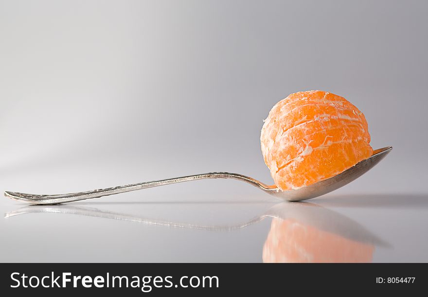 Metal teaspoon with a segment of tanregine in it, reflective surface, shadows