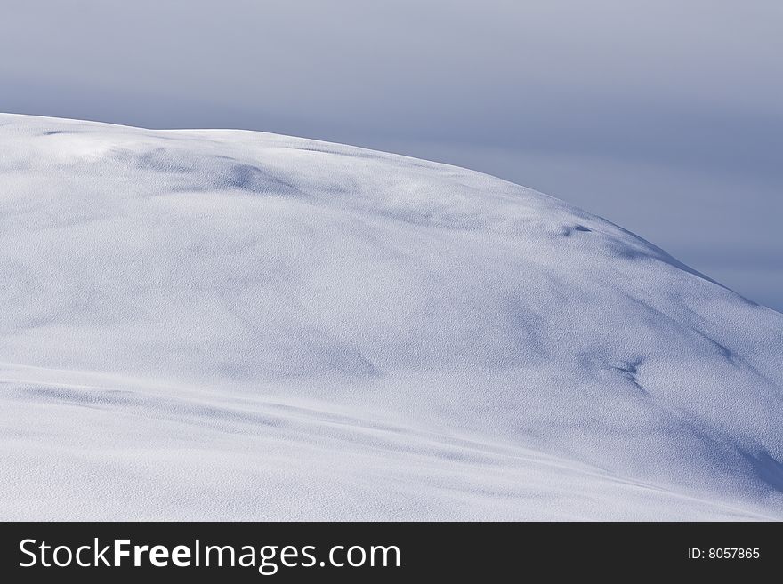 A view of an undulating and pristine snow covered hill. A view of an undulating and pristine snow covered hill