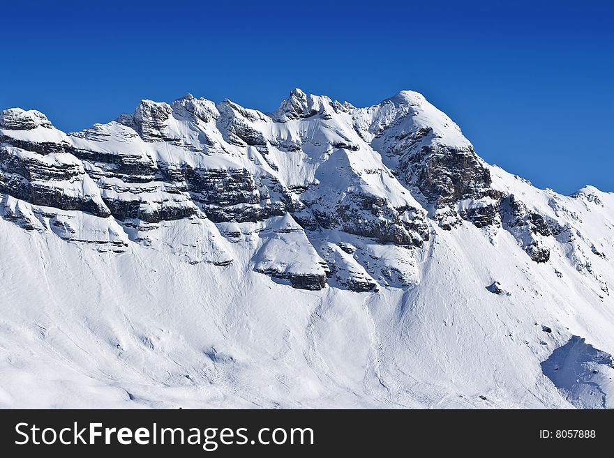 A view of a craggy, snow covered mountain range against a deep blue sky