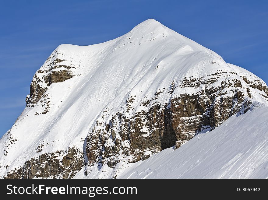 A view of a craggy, snow covered mountain peak against a deep blue sky