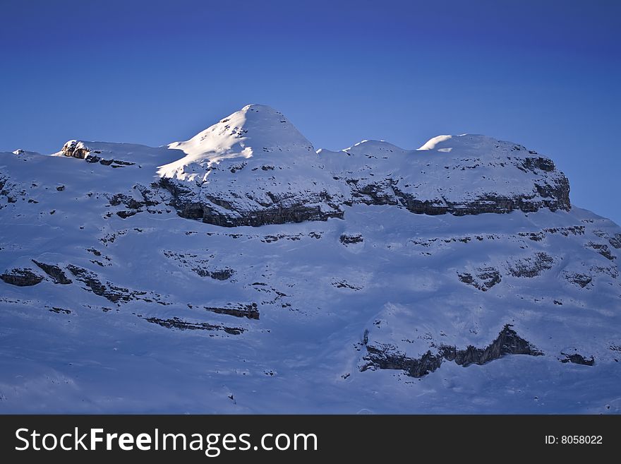 A view of a craggy, snow covered mountain peak against a deep blue sky