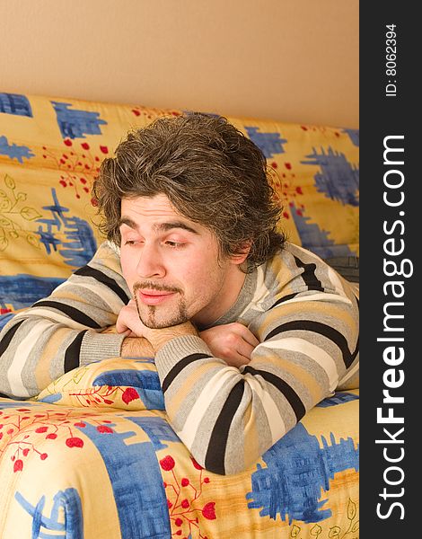 Young smiley dark haired caucasian man in striped sweater lying on country style sofa. Young smiley dark haired caucasian man in striped sweater lying on country style sofa