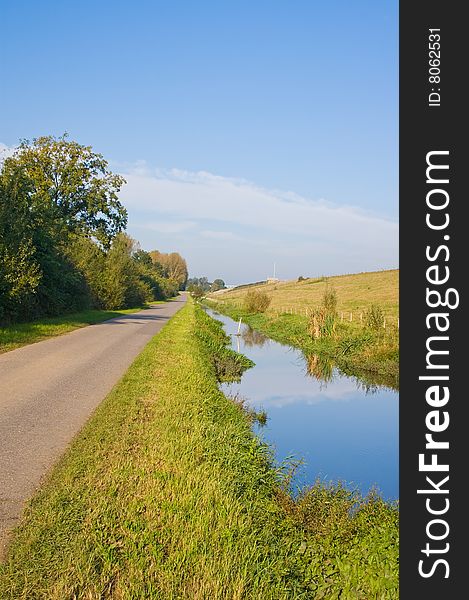 Green dike with a ditch and reflection in the water