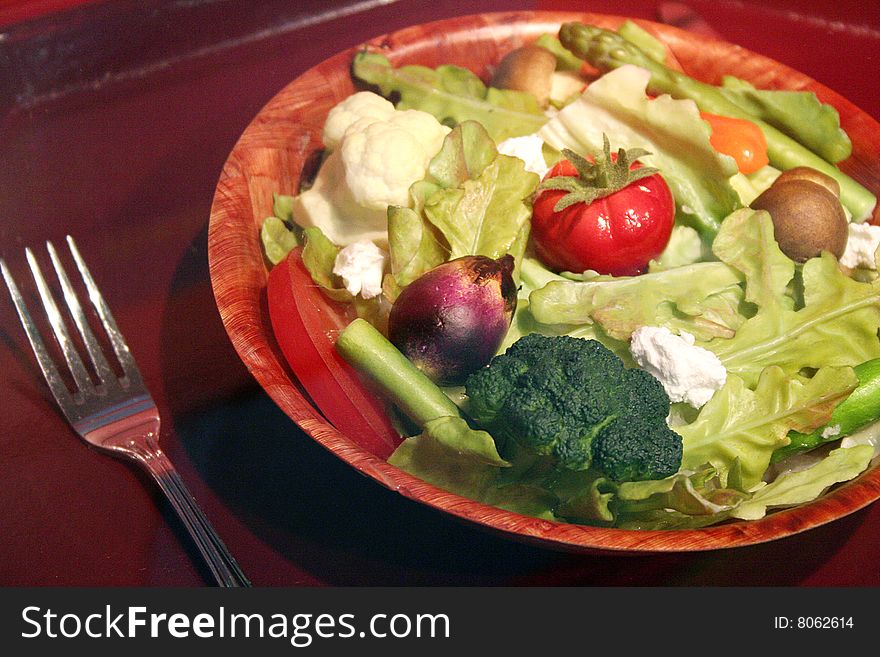 A fresh salad is full of vegetables with a fork nearby.