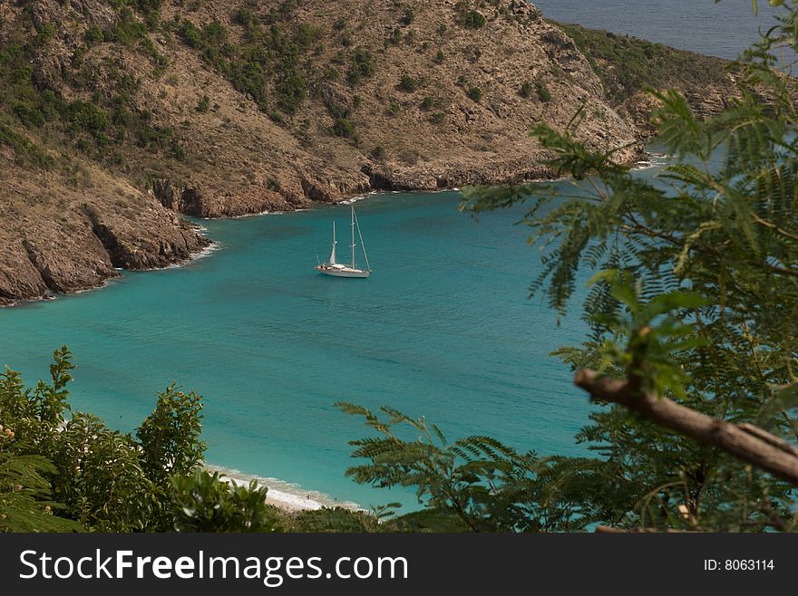 View from above of a tropical bay with a single sailboat at anchor. View from above of a tropical bay with a single sailboat at anchor.