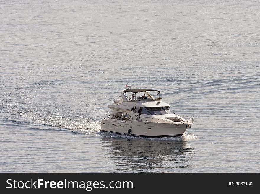 A white yacht cutting through the calm blue water of a bay. A white yacht cutting through the calm blue water of a bay