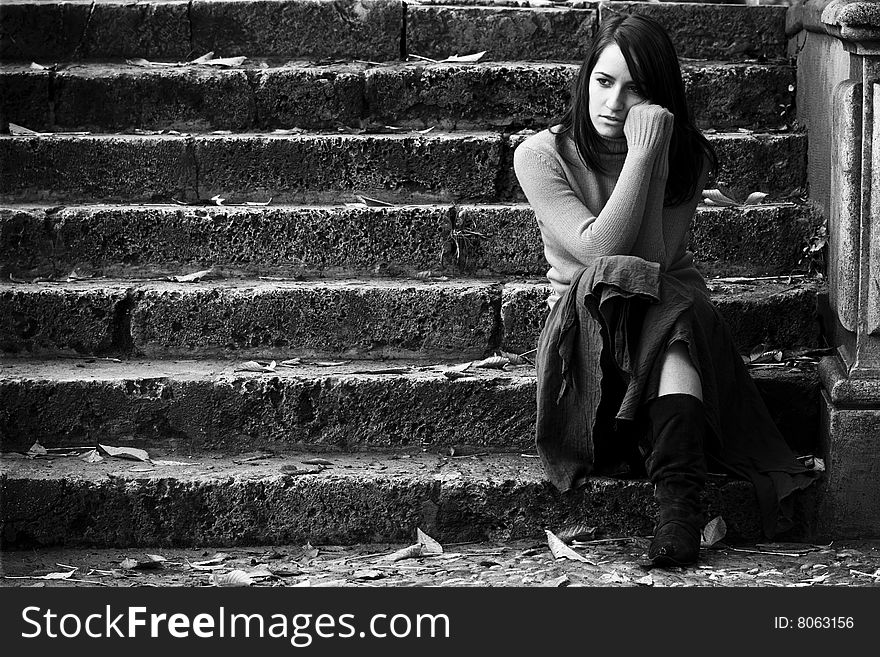 Young thoughtful woman sitting in stone stairs.