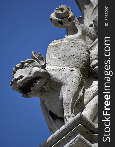 A frowning gargoyle hangs against the blue sky atop Notre Dame Cathedral in Paris, France. A frowning gargoyle hangs against the blue sky atop Notre Dame Cathedral in Paris, France.