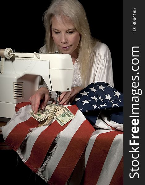 Attractive blond woman sewing American currency into the mending of a tattered American flag on a sewing machine. Attractive blond woman sewing American currency into the mending of a tattered American flag on a sewing machine.