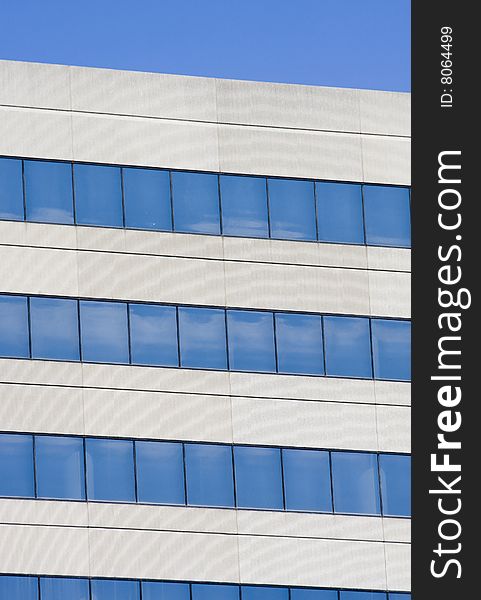 Details of a grey concrete building with blue windows reflecting sky. Details of a grey concrete building with blue windows reflecting sky