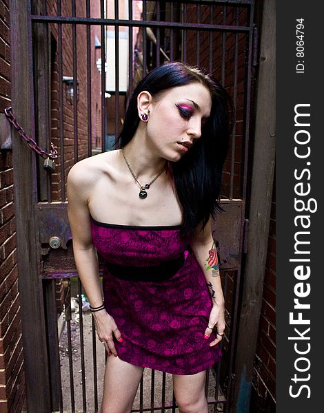 Pretty woman with jet black hair wearing a print sleeveless dress. She is standing in an alley in front of a chained fence. Pretty woman with jet black hair wearing a print sleeveless dress. She is standing in an alley in front of a chained fence.