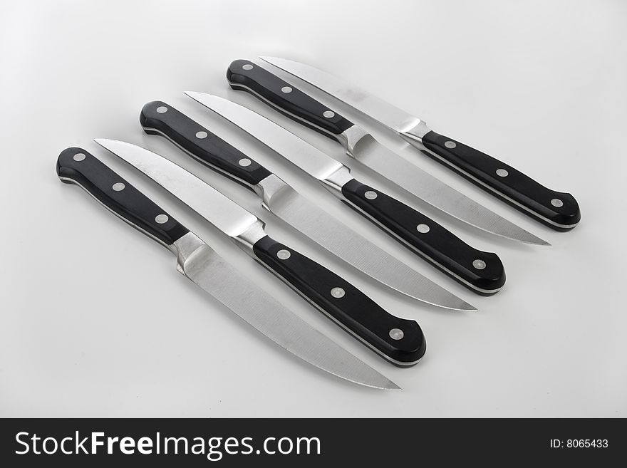 Four steak knives lined up on a white background