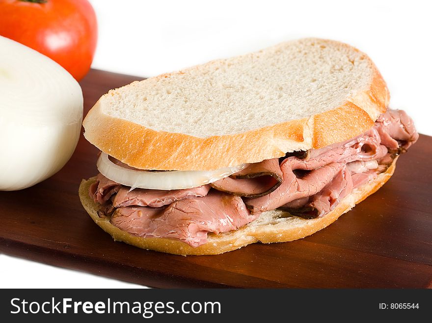 A roast beef sandwich on a wood cutting board presented with onion and tomato. A roast beef sandwich on a wood cutting board presented with onion and tomato