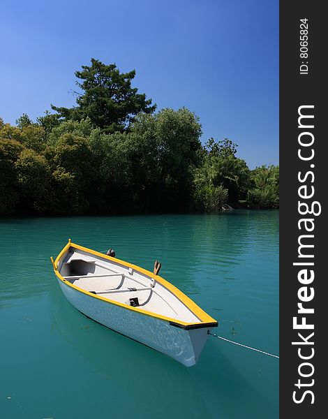 A clean white boat floating on a deep green river, trees and blue sky in background