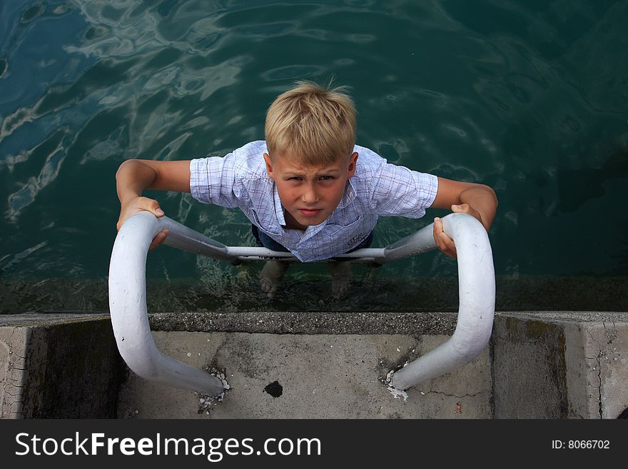 Young boy climbing ladder leading up from deep water