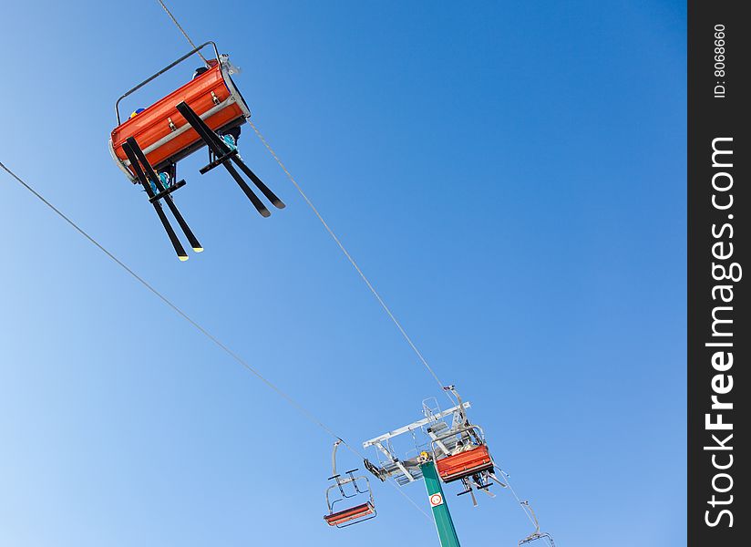 Skiers are riding in chairlift in a ski area, low angle view, Italy. Large copy-space at the top.