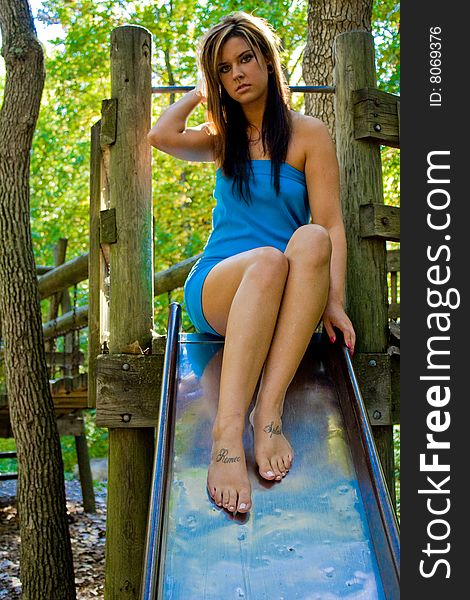 A tall girl on a slide at a playground in the woods. She is barefoot, revealing tattoos on the top of each foot. A tall girl on a slide at a playground in the woods. She is barefoot, revealing tattoos on the top of each foot
