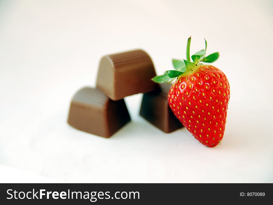 A red strawberry with three chocolates on white background. A red strawberry with three chocolates on white background