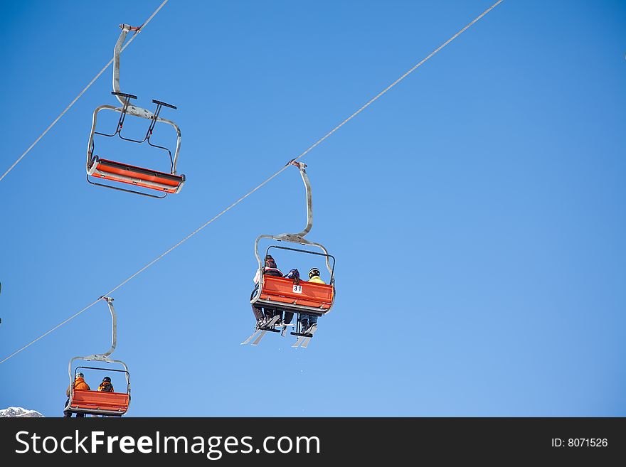 Skiers are riding in chairlift in a ski area, low angle view, Italy. Large copy-space at the top.