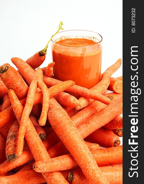 A glass of fresh carrot juice and a bunch of carrots in foreground. A glass of fresh carrot juice and a bunch of carrots in foreground.
