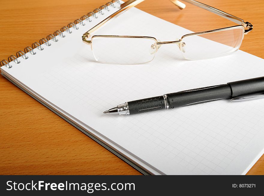 Notebook, glasses and pen on table