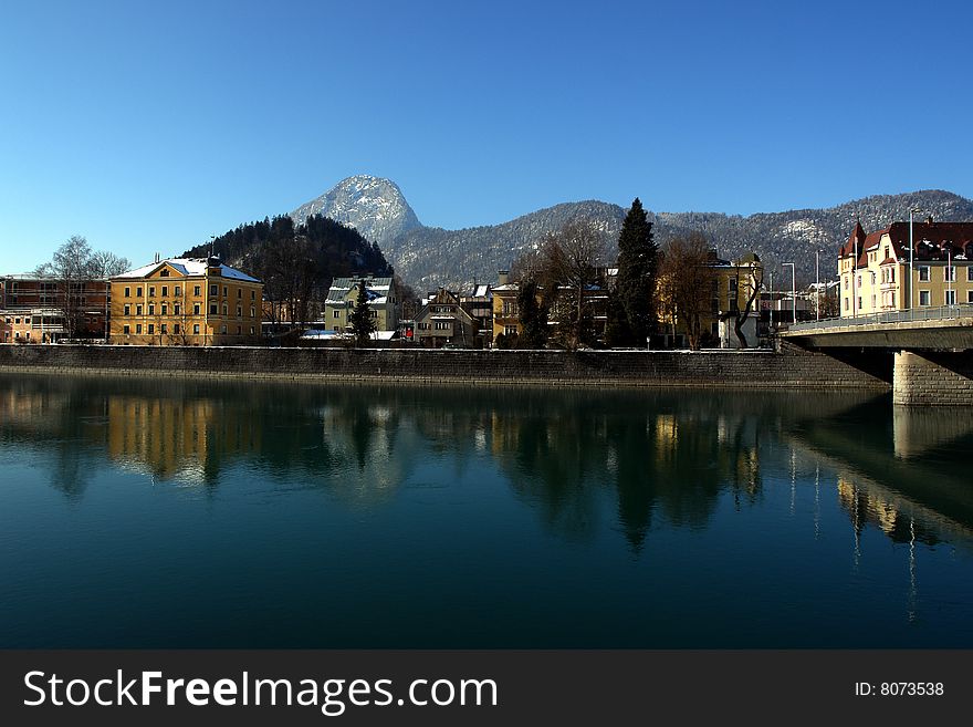 Inn River in Kufstein City , Tirol, Austria .
Buildings Mountains and blue sky is reflecting in blue water.