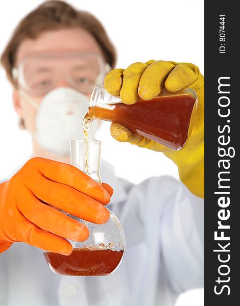 Scientist in respirator and rubber gloves pours  brown liquid from one flask in another. Scientist in respirator and rubber gloves pours  brown liquid from one flask in another