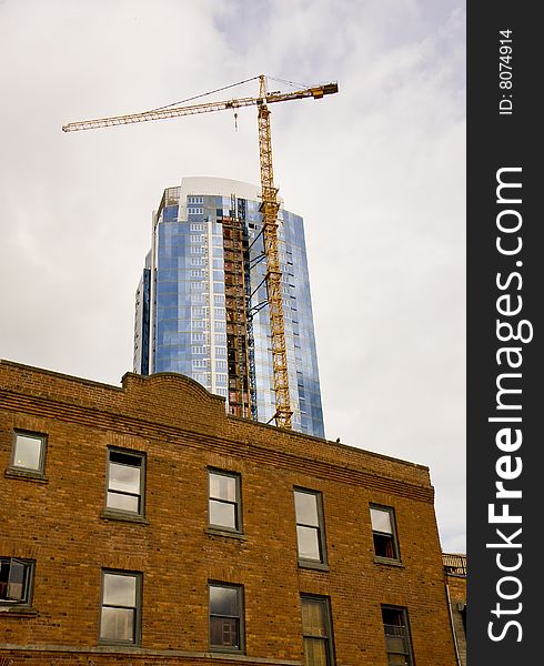 A modern glass tower being built behind an old brick building. A modern glass tower being built behind an old brick building