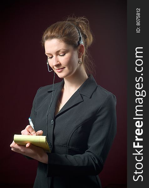 Beautiful Secretary Wearing Headset Taking Dictating Notes on yellow notepad with a dark background. Beautiful Secretary Wearing Headset Taking Dictating Notes on yellow notepad with a dark background