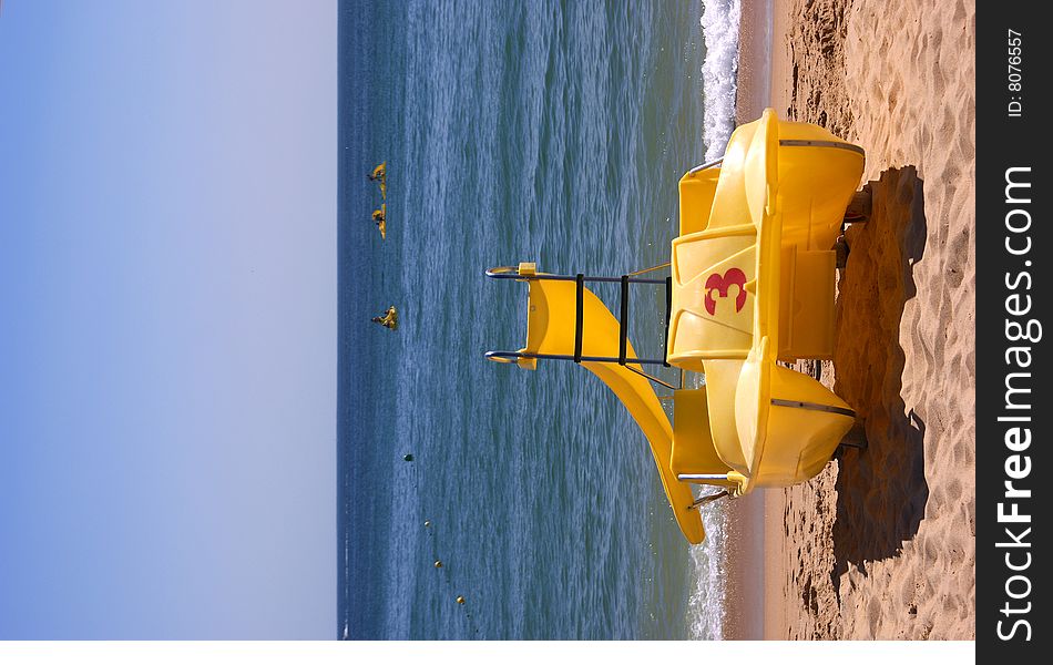 Yellow pedalboat on a sandy beach with the ocean in the background. Yellow pedalboat on a sandy beach with the ocean in the background