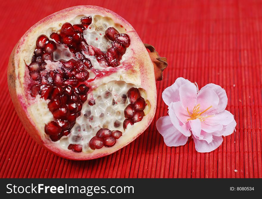 Slice of sweet pomegranate and flower on red background. Slice of sweet pomegranate and flower on red background