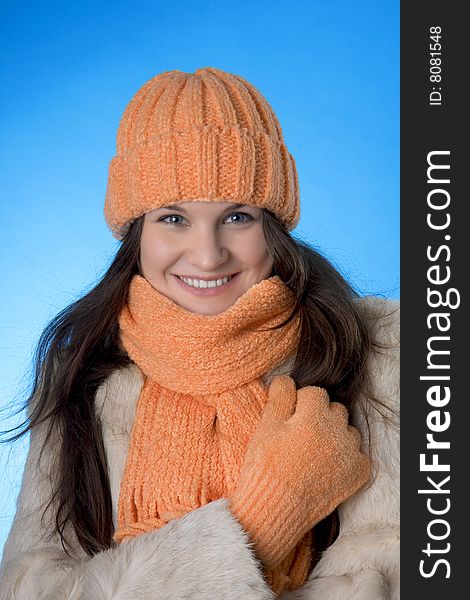 Picture of a beautiful brunette girl in the orange cap and coat on a blue background